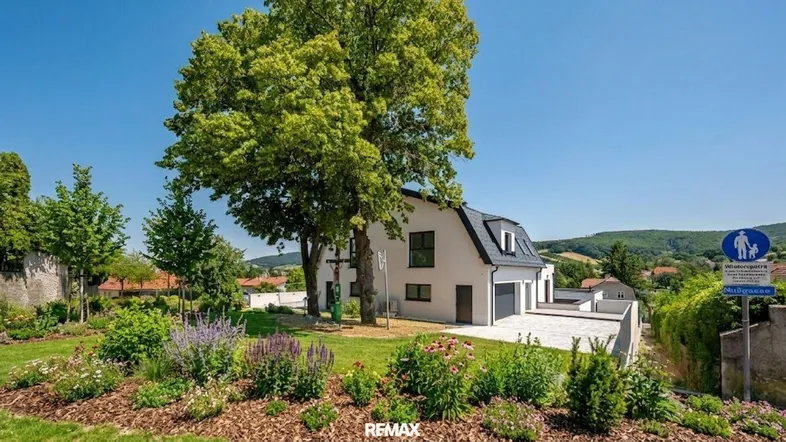 Modernes Einfamilienhaus mit gepflegtem Garten, großen Bäumen und weitem Blick ins Grüne.