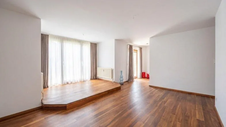 Helles, leeres Wohnzimmer mit Holzboden und Zugang zu großen Fenstern.