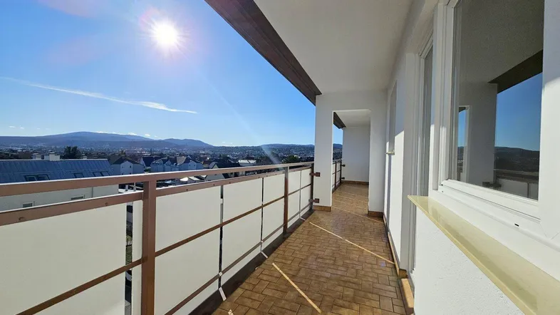 Sonniger Balkon mit Fliesenboden und weitem Blick über die Stadt und die umliegenden Berge.