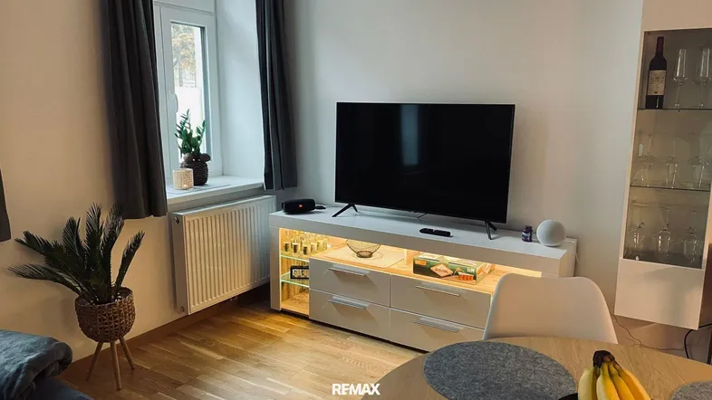 Heller Wohnbereich mit Fernseher, modernem Sideboard und Holzboden nahe einem Fenster.