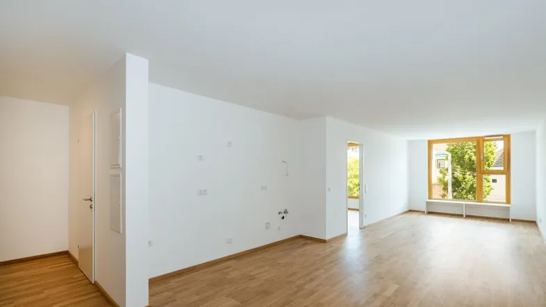 Heller, leerer Raum mit Parkettboden und großen Fenstern, ideal für einen offenen Wohnbereich.