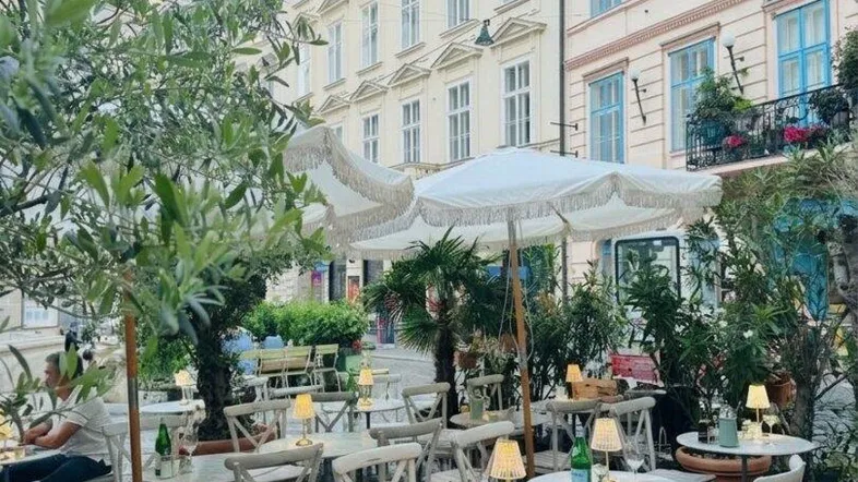 Gemütlicher Außenbereich eines Restaurants mit Tischen, Stühlen und Sonnenschirmen in einer belebten Straße.