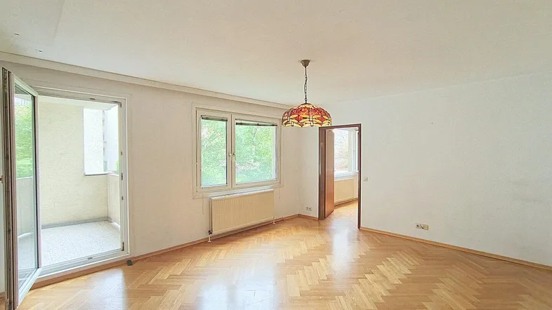Helles Wohnzimmer mit Fischgrätparkett und Zugang zu einem kleinen Balkon, bietet viel Tageslicht.