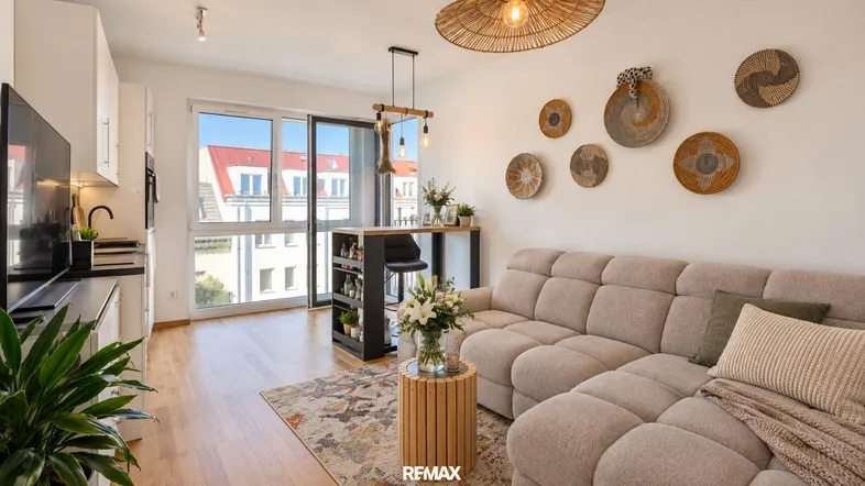 Helles, offenes Wohnzimmer mit integrierter Küche, Holzboden und Zugang zum Balkon.