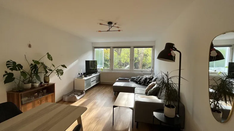 Helles Wohn- und Esszimmer mit Holzboden, bequemer Couch und Blick ins Grüne.