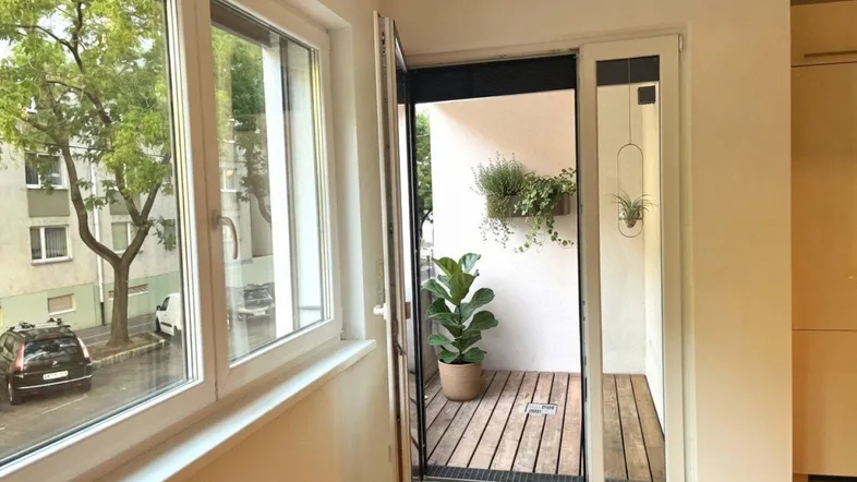 Heller Wohnbereich mit Holzboden und Zugang zu einem kleinen Balkon mit Pflanzen.
