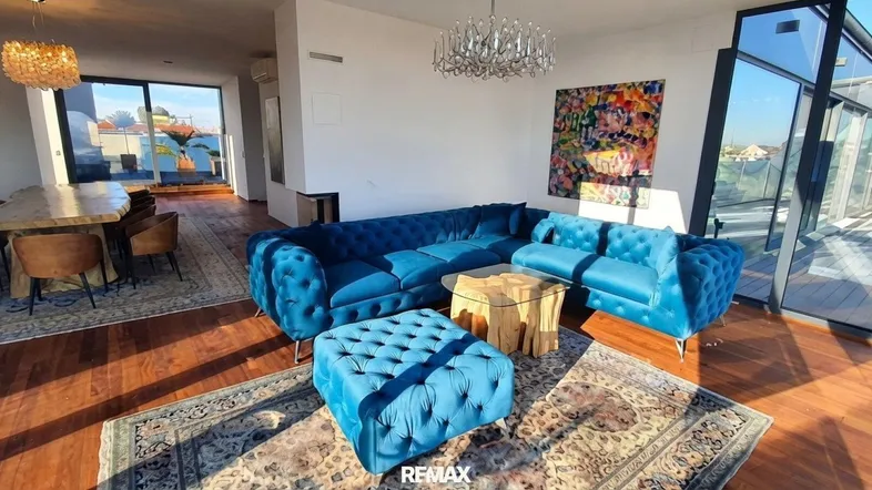 Geräumiger Wohn- und Essbereich mit blauen Samtsofas, Holzboden und Zugang zur Terrasse.