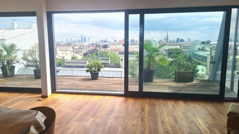Helles Wohnzimmer mit Holzboden, großen Fenstern und weitem Stadtblick über die Dächer.