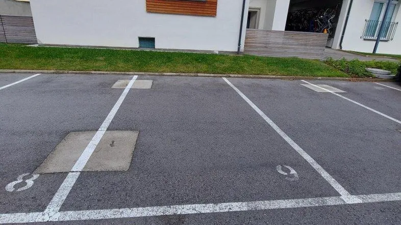 Außenansicht eines modernen Wohngebäudes mit Holzverkleidung und asphaltiertem Parkplatz.