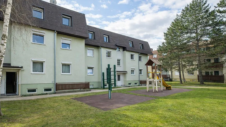 Mehrfamilienhaus mit heller Fassade, Spielplatz und Grünflächen im Gemeinschaftsgarten.