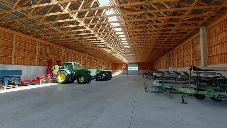 Geräumige Lagerhalle mit hoher Holzkonstruktion und Betonboden, ideal für landwirtschaftliche Maschinen.