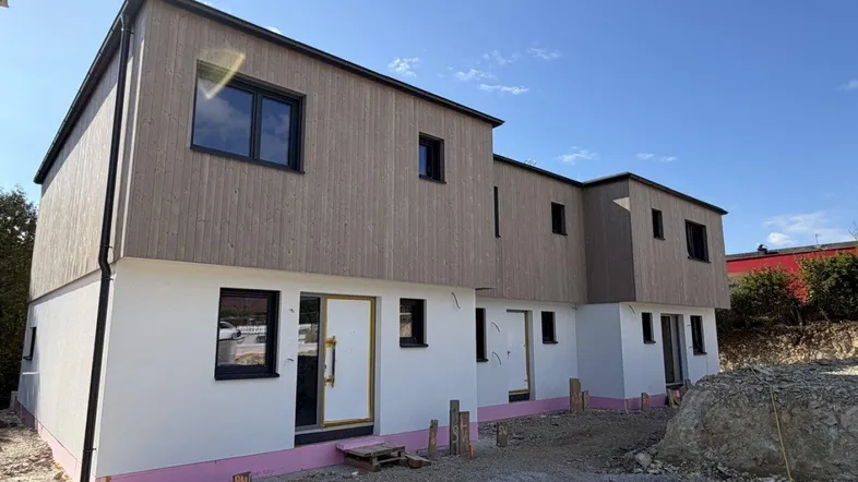 Modernes Neubaugebäude mit Holzfassade und weißem Putz, noch im Bau befindlich.