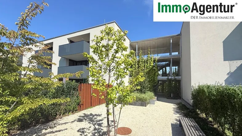 Modernes Mehrfamilienhaus mit gepflegtem Kiesweg und Sitzbank im Außenbereich unter blauem Himmel.