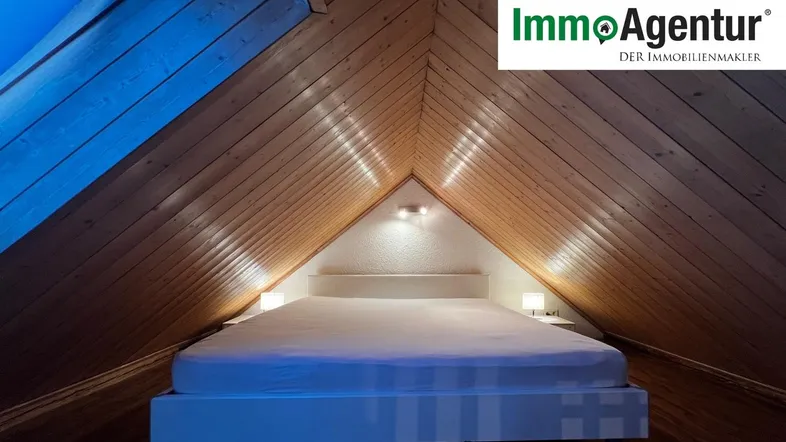 Gemütliches Schlafzimmer im Dachgeschoss mit Holztäfelung und schräger Decke.