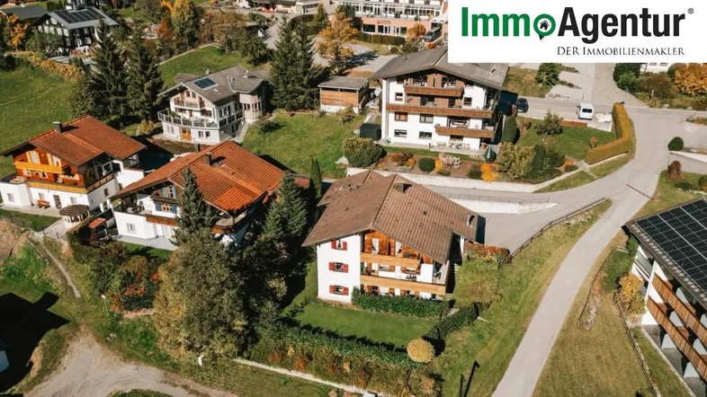 Luftaufnahme einer Wohnsiedlung mit mehreren Häusern und grünen Gärten in alpiner Umgebung.