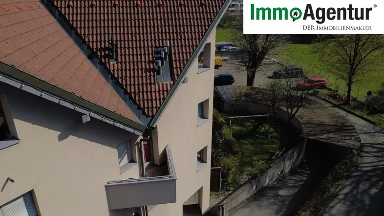 Luftaufnahme eines gepflegten Wohnhauses mit Ziegeldach, beiger Fassade und kleinen Balkonen in grüner Umgebung.