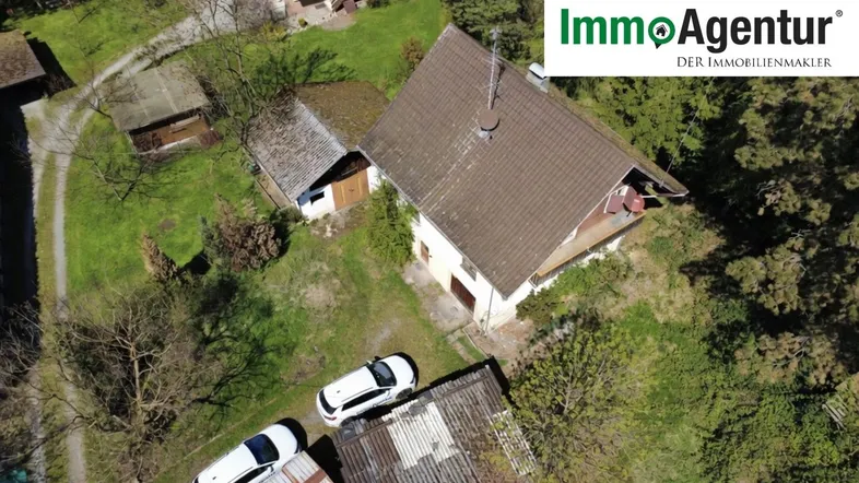 Luftaufnahme eines Einfamilienhauses mit Satteldach und umliegendem Grundstück, inklusive Maklerlogo.