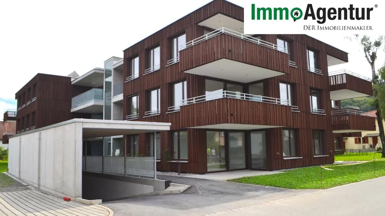 Modernes Mehrfamilienhaus mit Holzfassade und Tiefgaragenzufahrt in einer grünen Umgebung.