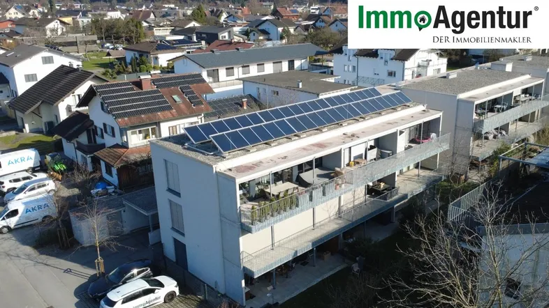 Modernes Mehrfamilienhaus mit Solaranlage auf dem Dach, umgeben von Wohnbebauung und grüner Landschaft.