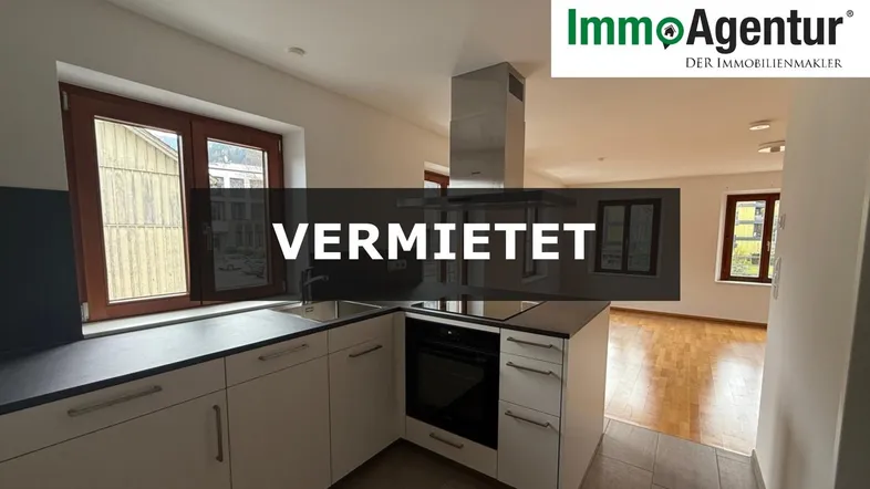 Moderne Einbauküche mit Kochinsel, dunkler Arbeitsplatte und Blick nach draußen durch die Fenster.
