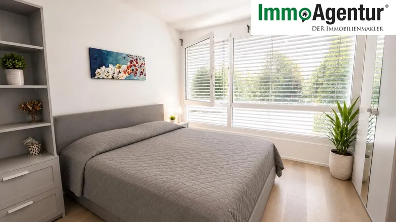 Helles Schlafzimmer mit großem Bett, Holzfußboden und Blick ins Grüne durch die Fenster.