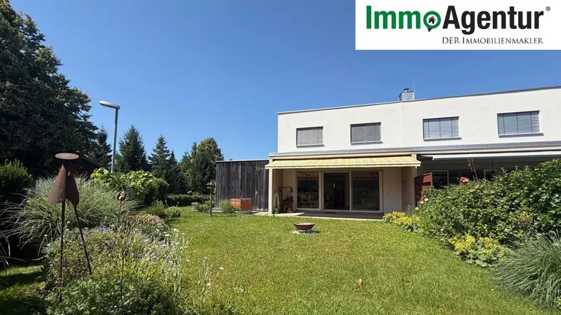 Geräumiger Garten hinter dem Haus mit Rasenfläche und Blumenbeeten unter blauem Himmel.