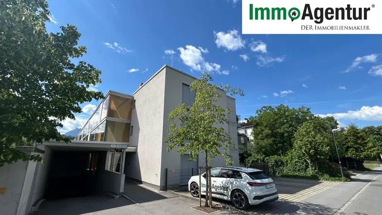 Modernes Gebäude mit klarer Architektur, überdachtem Eingangsbereich und Parkplatz im Freien.