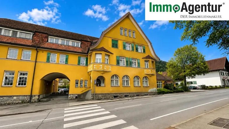 Gelbes Gebäude mit traditioneller Architektur, grünen Fensterläden und einer Straße im Vordergrund.