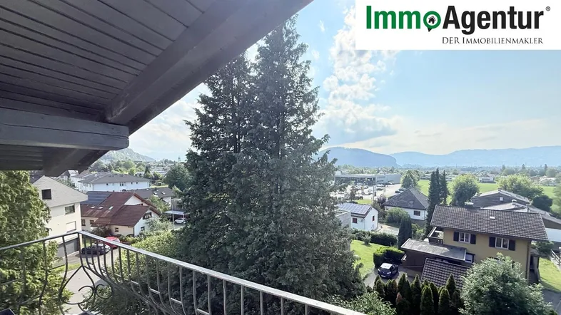 Sonniger Balkon mit schmiedeeisernem Geländer und weitem Blick über die Wohngegend und Berge.