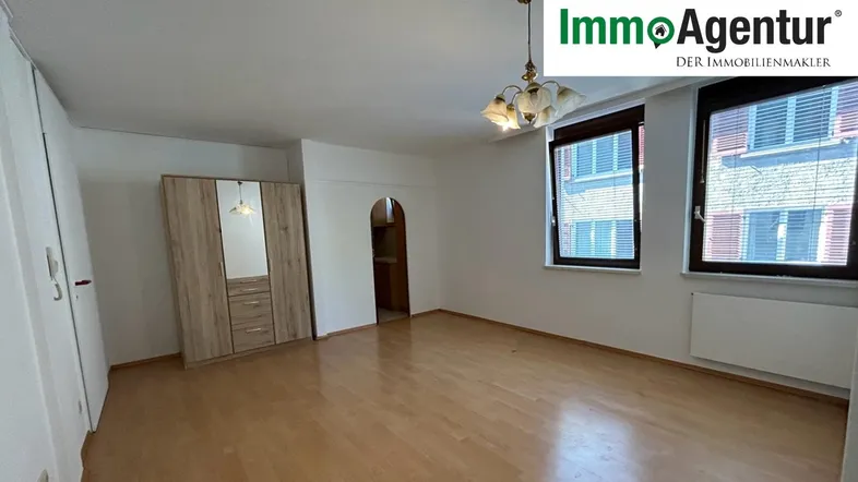 Heller Wohnraum mit Laminatboden, zwei Fenstern und einem Kleiderschrank.