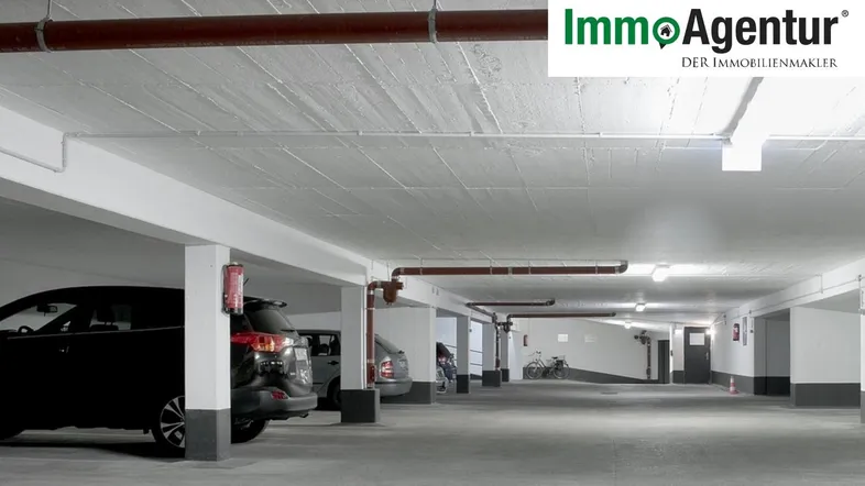 Geräumige Tiefgarage mit mehreren Stellplätzen, Betonboden und sichtbaren Leitungen an der Decke.