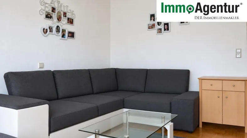 Gemütliches Wohnzimmer mit L-förmigem Sofa, Glastisch und hellem Holzschrank.