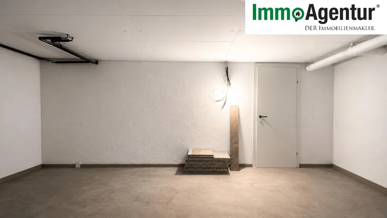 Leerer Raum mit weißen Wänden, Betonboden und sichtbaren Installationen, ideal als Keller oder Abstellraum.