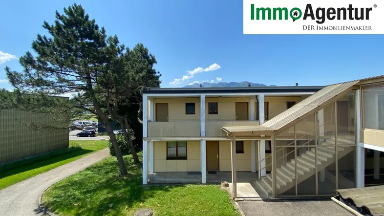 Mehrstöckiges Gebäude mit externer Treppe und Blick auf die umliegende Landschaft und Berge unter blauem Himmel.
