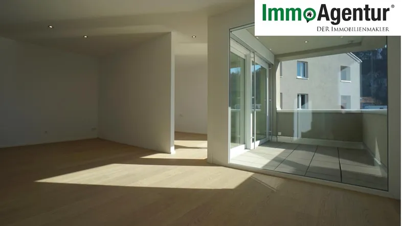Heller, leerer Wohnbereich mit Holzboden und Zugang zu einem Balkon, durchflutet von natürlichem Licht.