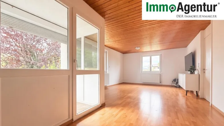 Helles Wohnzimmer mit Holzbalkendecke, Parkettboden und Zugang zu einem Balkon.