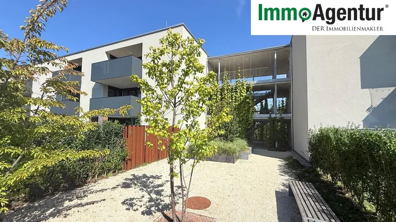 Moderner Apartmentkomplex mit gepflegtem Innenhof und Sitzgelegenheiten unter blauem Himmel.