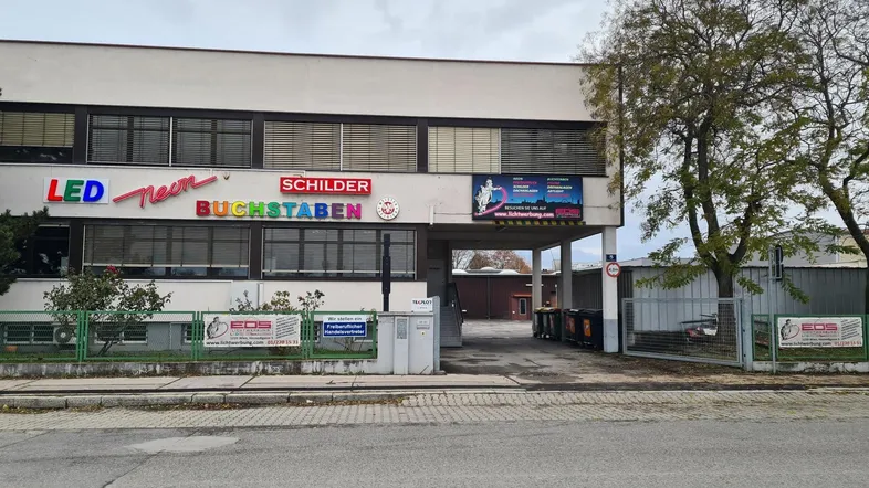 Ansicht eines Gewerbegebäudes mit auffälliger LED-Neon-Beschilderung und Zufahrt zum Hinterhof.
