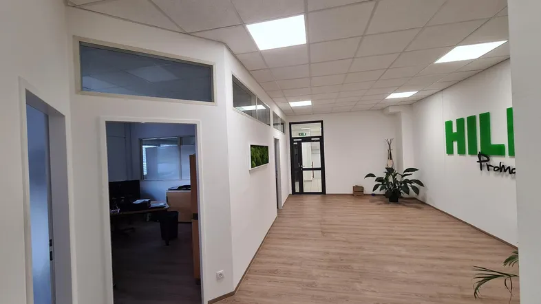 Heller Bürobereich mit modernem Laminatboden, weißen Wänden und Zugang zu weiteren Büroräumen.