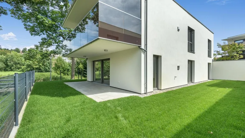 Moderne Architektur mit großer Rasenfläche und gepflasterter Terrasse am Haus.