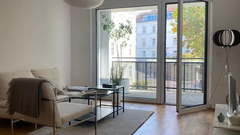 Helles Wohnzimmer mit Holzboden, modernen Möbeln und Zugang zu einem Balkon.