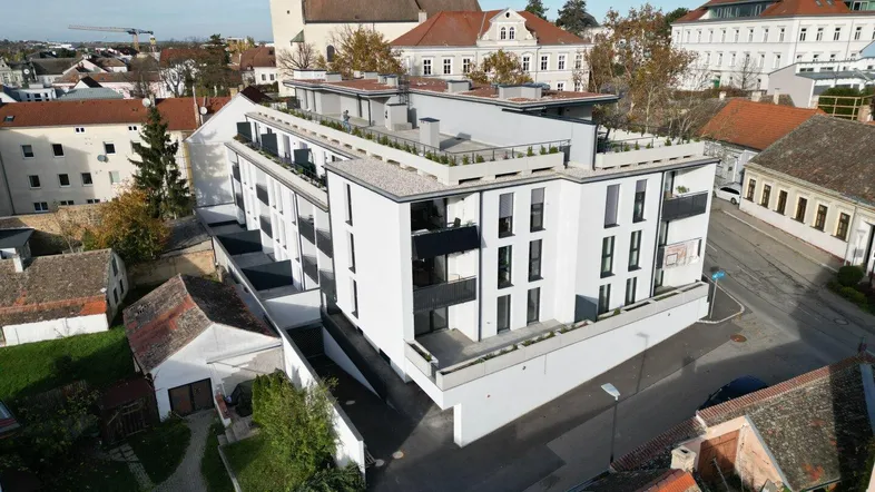 Moderne Wohnanlage mit Flachdach und begrünten Terrassen in städtischer Umgebung mit Kirchturm.