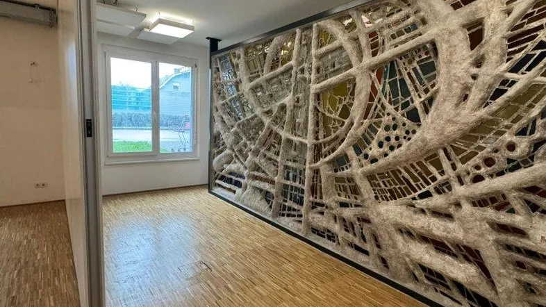 Heller Innenraum mit Holzboden, großen Fenstern und einer dekorativen Trennwand mit komplexem Muster.