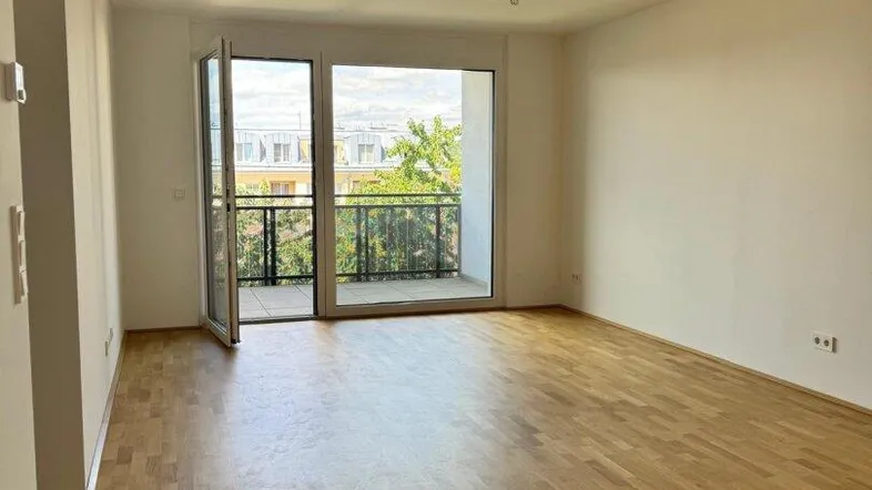 Helles, leeres Wohnzimmer mit Parkettboden und direktem Zugang zu einem Balkon.