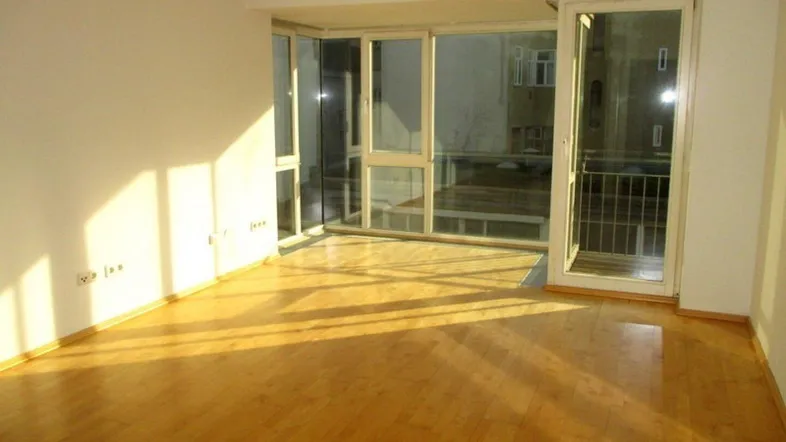 Helles Wohnzimmer mit Parkettboden und großen Fenstern, die viel Sonnenlicht hereinlassen.