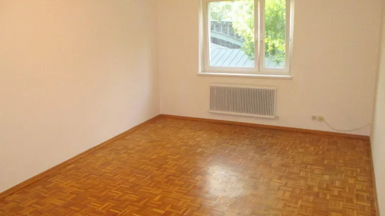Helles Zimmer mit Parkettboden und Fensterblick ins Grüne, ausgestattet mit einem Heizkörper.