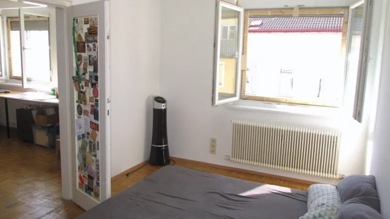 Helles Schlafzimmer mit Holzboden, großem Fenster und Zugang zu einem weiteren Raum.