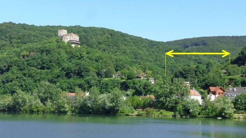 Panoramablick auf den See mit bewaldeten Hügeln und einer historischen Burg im Hintergrund.