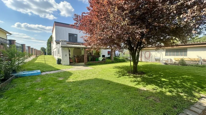Geräumiger Gartenbereich mit gepflegtem Rasen, einem großen Baum und einer überdachten Terrasse am Haus.