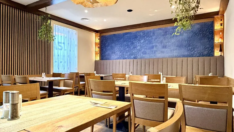 Speisesaal mit Holztischen, bequemen Stühlen und blauer Akzentwand.